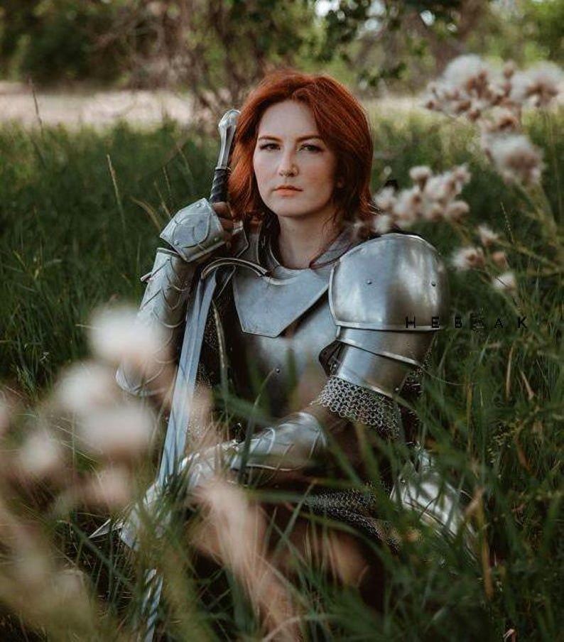Back view highlighting the steel chainmail and full leg armor including greaves, worn as part of a full-body female knight costume.