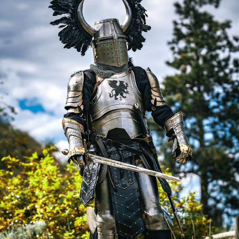 Close-up of the steel horned helmet featuring black feather plumes and full facial protection, included in the Griffin Knight armor set.