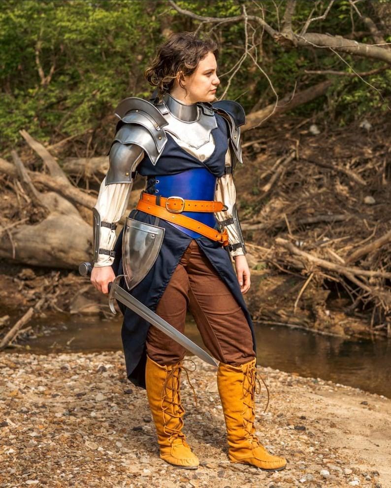 Close-up of polished steel pauldrons and gorget showing elegant curvature and riveted detailing for a heroic female warrior look.