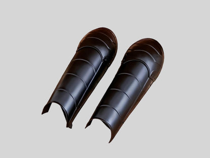 Blackened steel leg greaves with adjustable leather straps for reenactment armor costume