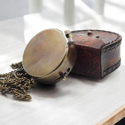 Brass pocket compass placed inside engraved leather case.

