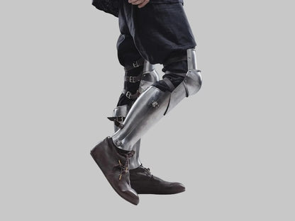 Polished steel medieval leg greaves with knee cap protection detail showing authentic Gothic knight armor craftsmanship